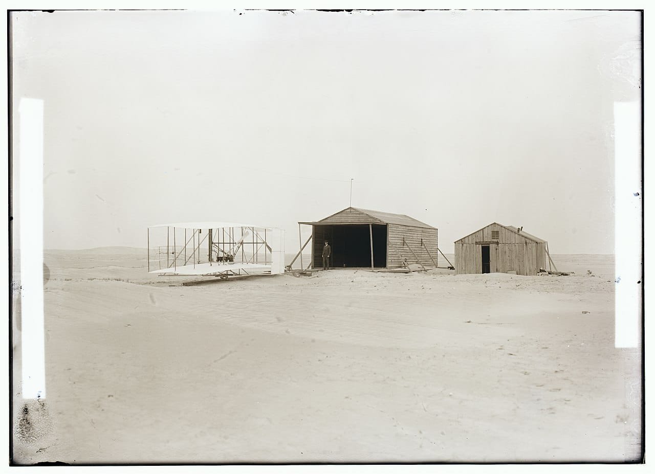 The 1903 Wright Flyer in front of the Wright Brothers camp buildings at Kill Devil Hills