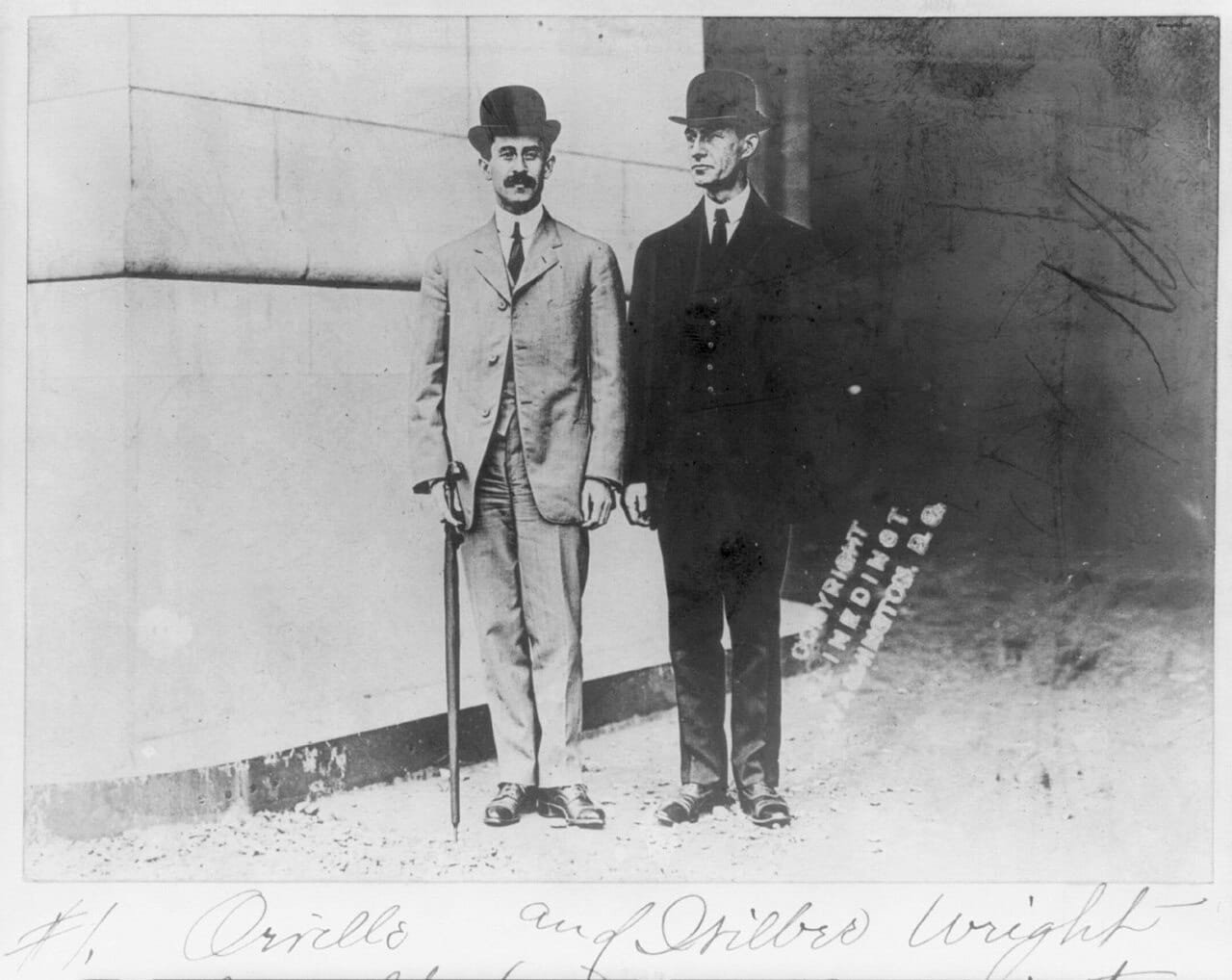 Full length portrait of Wilbur and Orville Wright wearing derby hats