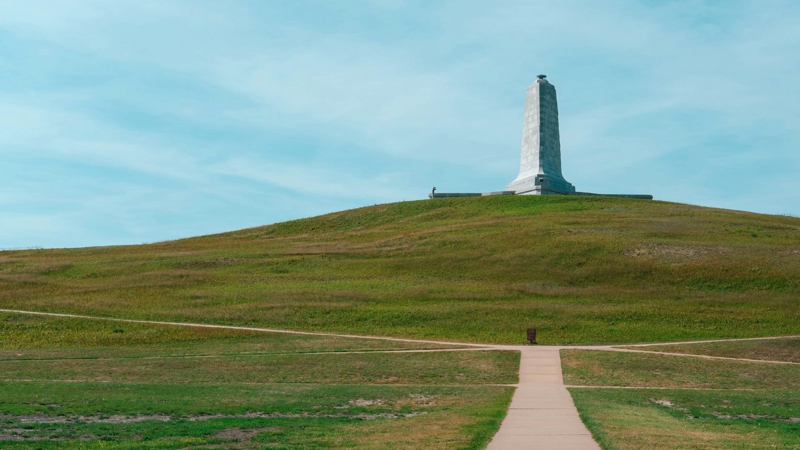 A paved footpath running up the grassy slope of Kill Devil Hill toward the Wright Brothers Memorial standing on the crest.
